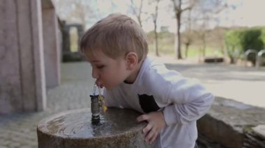 Anne ve çocuk parktaki taştan bir fıskiyeden su içerek kendilerini yeniliyorlar.