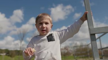 Genç bir çocuk güneşli bir günde elinde metal bir merdivenle muzdan zevk alıyor.