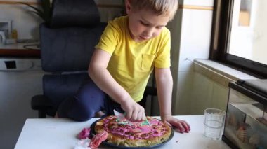 Çocuk renkli kremayla bir doğum günü pastasını dikkatlice dekore ediyor.