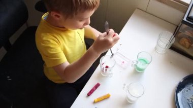 Anaokulu öğrencisi renkli balmumunu kaşıkla karıştırıyor.