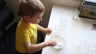 Masadaki kasede beyaz bir maddeyi karıştıran ve yiyen genç bir çocuk.