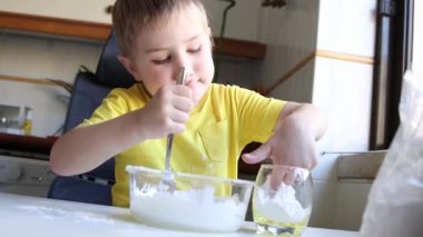 Genç bir çocuk cam bir kâseye beyaz malzemeleri karıştırıyor.