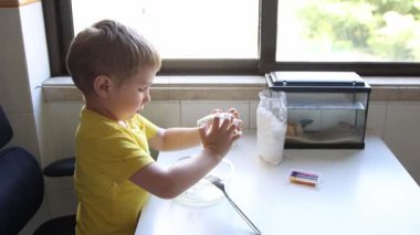 Meraklı çocuk, malzemeleri kaseye doldurup, parlak mutfakta pişirmeye hazırlanıyor.
