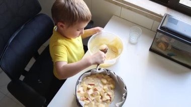 Genç çocuk dilimlenmiş elmaların üzerine dikkatlice hamur dökerek lezzetli bir elmalı turta hazırlıyor.