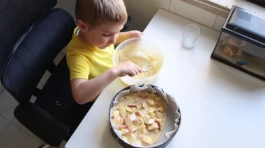 Genç çocuk dikkatli bir şekilde kek hamuruna elma dilimleri yerleştiriyor, lezzetli bir tatlı hazırlıyor.