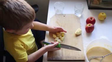 Çocuk dikkatli bir şekilde tahta tahtada elma keserek sağlıklı bir atıştırmalık hazırlıyor.