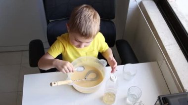 Mutfakta yemek tarifi hazırlayan konsantre çocuk kasede malzemeleri çırpıyor.