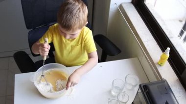 Çocuk yemek yapmayı öğreniyor. Malzemeleri beyaz bir masada karıştırıyor.