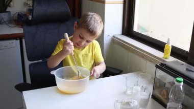 Mutfak masasında oturan şeffaf bir kasede konsantre çocuk malzemeleri çırpıyor.