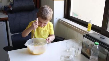 Çocuk çanakta malzeme çırpıyor, yemek yapmayı öğreniyor.