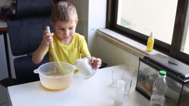 Çocuk dikkatli bir şekilde yemek yapmayı öğreniyor kaseye malzeme ekleyerek ve çırparak.