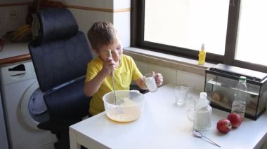 Çocuk elma suyu malzemelerini karıştırıyor, beyaz bir masada oturuyor.