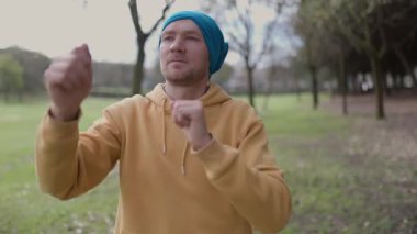 Genç adam parkta gölge boksu yapıyor.