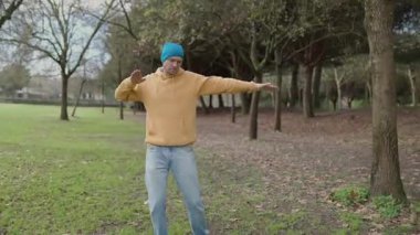 Yeşil bir parkta tai chi chuan yapan sıradan giyinmiş bir adam.