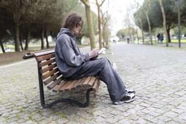 Öğrenci, parkta bir bankta oturup temiz havanın ve sessiz ortamın tadını çıkarıyor.