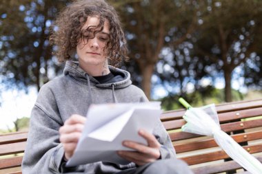 Genç sanatçı bir bankta otururken deftere notlar yazıyor.