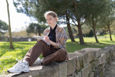 Konsantre olmuş kız öğrenci parkta ders çalışmaktan zevk alıyor.