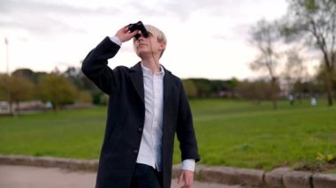 Genç dedektif parkta yürüyor ve dürbün kullanıyor.