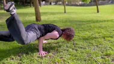 Genç break dansçı parkta çimlerin üzerinde hareket ediyor.