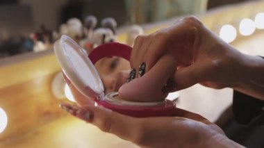 Gösteriden önce soyunma odasında makyaj süngeriyle sıvı fondöten süren bir kadın.