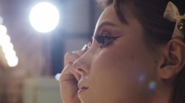 Soyunma odasındaki aynaya göz kalemi süren genç bir kadın.