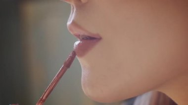 Profesyonel fırça aplikatörüyle sıvı ruj süren genç bir kadının yan görüntüsü.