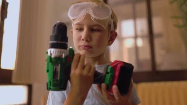 Güvenlik gözlüğü takan, elinde matkap tutan ve kameraya gülümseyen genç bir çocuk.