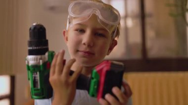 Güvenlik gözlüğü takan meraklı küçük çocuk evde kablosuz matkap kullanmayı öğreniyor.