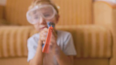 Koruyucu gözlük takan sevimli küçük çocuk evde plastik testereyle tahta görmüş gibi yapıyor.