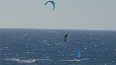 14 Haziran 2023 - Lizbon, Portekiz, Guincho plajı: iki adam mavi okyanusta uçurtma ve rüzgar sörfü yapıyor. Orta çekim