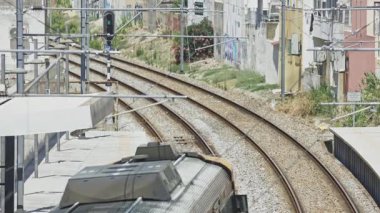 Bir istasyon platformunun yanındaki kıvrımlı raylarda giden bir trenin yüksek açılı görüntüsü