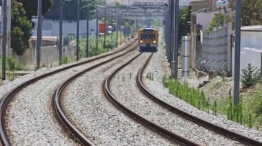 Parlak farları olan banliyö treni bir şehir bölgesinden geçen demiryolu raylarına yaklaşıyor.