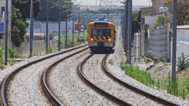 Sarı yolcu treni, yaz mevsiminde bir banliyö bölgesinden geçen dolambaçlı bir demiryolu hattına yaklaşıyor.