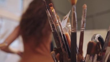 Önlük bağlayan, sanat atölyesinde resim yapmaya hazırlanan genç bir kadının arka plan görüntüsü.