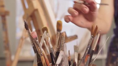 Resim stüdyosunda yaratıcı bir kadın boya fırçası seçiyor ve resim yapmaya başlıyor.