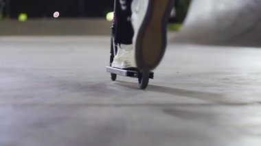 Geceleri beton bir kaykay parkında scooter kullanan insanların bacaklarını ve ayaklarını kapatın.