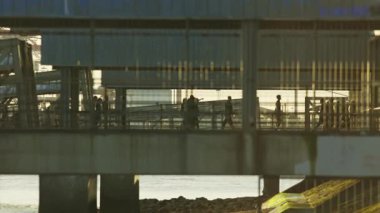 Yoğun bir şehirde, parlak ve sıcak bir ışığa karşı modern bir geçitten geçen isimsiz insanlar.