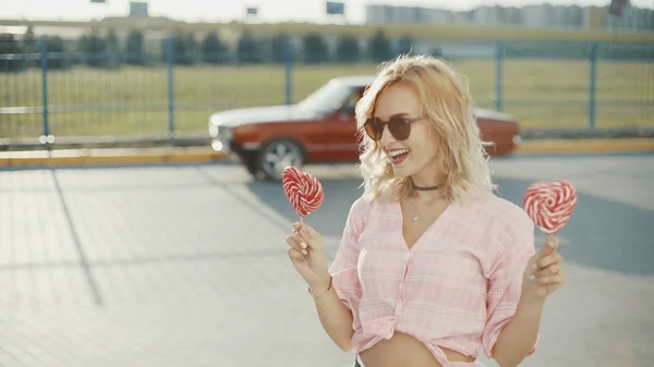 Beautiful young happy woman on the street with two colored lollipop at sunset