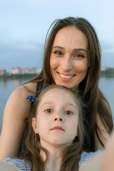 Mom and daughter take selfies and look directly at the camera. They are smile beautifully and seem happy.