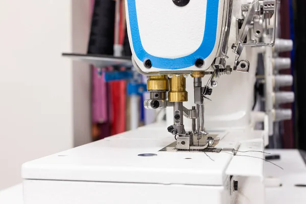 Atölyede profesyonel bir dikiş makinesi var. Çeşitli aygıtların arka planına ve bir terzinin iş eşyası ve araçları için gereksinimlerine karşı