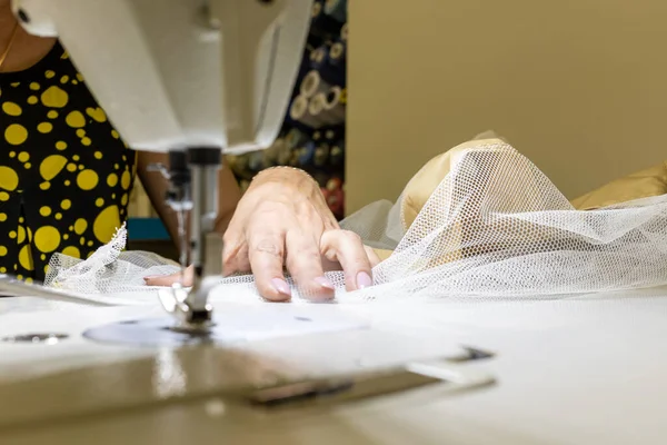 Kadın eli, atölyede profesyonel bir dikiş makinesinin önünde kumaşı tutar.