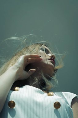 Şehir binasının arka planında poz veren güzel beyaz bir kız. Kız beyaz bir takım elbise giyiyor. Çok güzel saçları ve makyajı var.