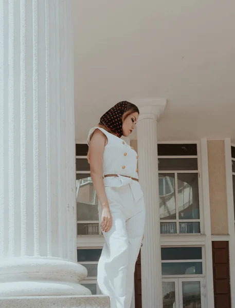Uma linda menina branca posando no fundo de um prédio da cidade. A menina está vestida com um terno branco. Ela tem cabelo lindo e maquiagem — Fotografia de Stock