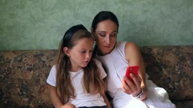 Anne ve kızı kanepede oturup kırmızı telefona bakıyorlar ve neler olduğunu duygusal olarak tartışıyorlar.