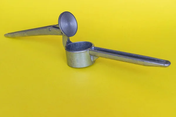 Sarımsak doğramak için çelik bir el presi parlak, zıt sarı bir arka planda yatar.