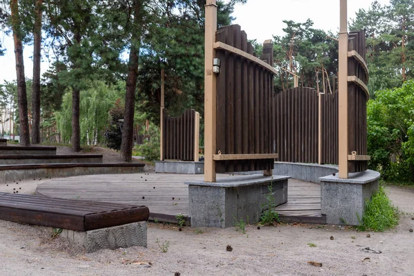 Ahşap kaplama ve önünde banklar olan yarı dairesel bir sahne. Park ve yoğun bitki örtüsü arka planda