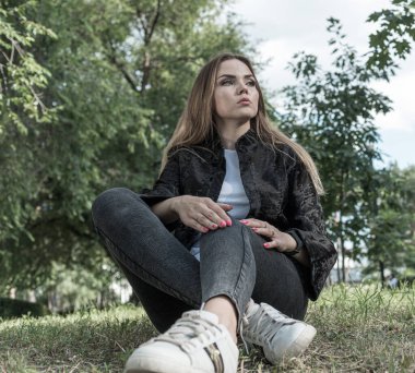 Uzun saçlı ve anlamlı gözlü güzel bir kız parkta kürk giymiş poz veriyor.