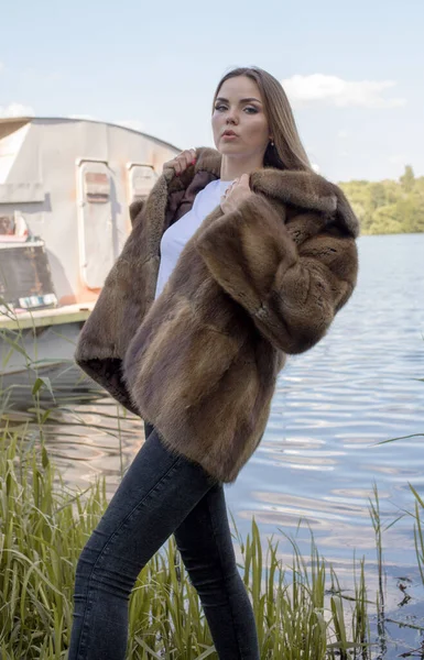 Uzun saçlı ve anlamlı gözlü güzel bir kız parkta kürk giymiş poz veriyor.