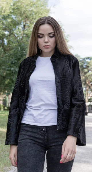 Uzun saçlı ve anlamlı gözlü güzel bir kız parkta kürk giymiş poz veriyor.