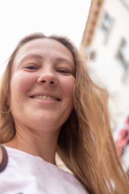 Beyaz tişörtlü ve kot pantolonlu güzel bir kız şehrin sokaklarında poz veriyor. Uzun saçları var ve makyajı yok. Eski şehrin mimarisi onun etrafında bir zemin.